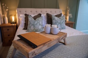 A neatly made bed with a wooden tray holding a book titled "The Family Tree" and two white ceramic cups.