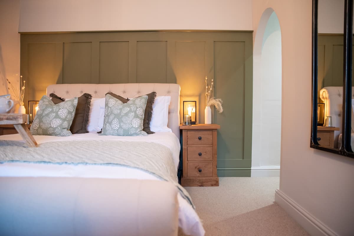 A bedroom with a bed, a nightstand, a mirror, and a wall with a decorative arch.
