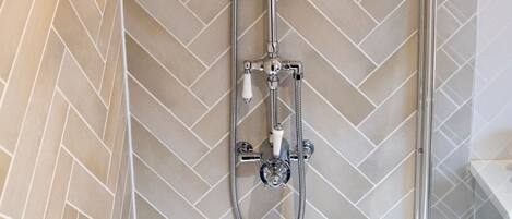 A shower with a rain showerhead and handheld showerhead, a glass door, and a herringbone-patterned tile wall.