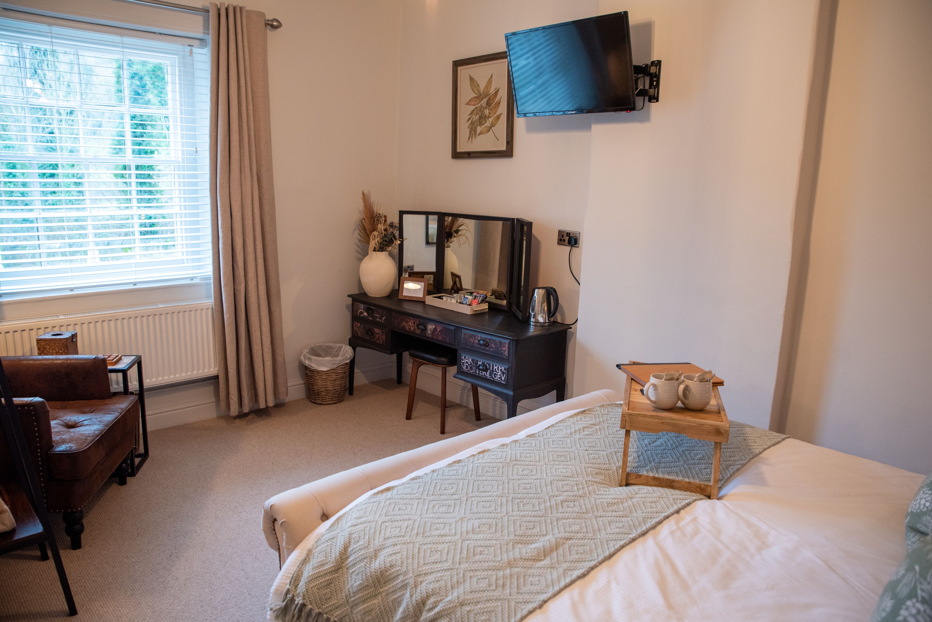 A bedroom with a bed, a desk with a mirror, a television, and a window with curtains.