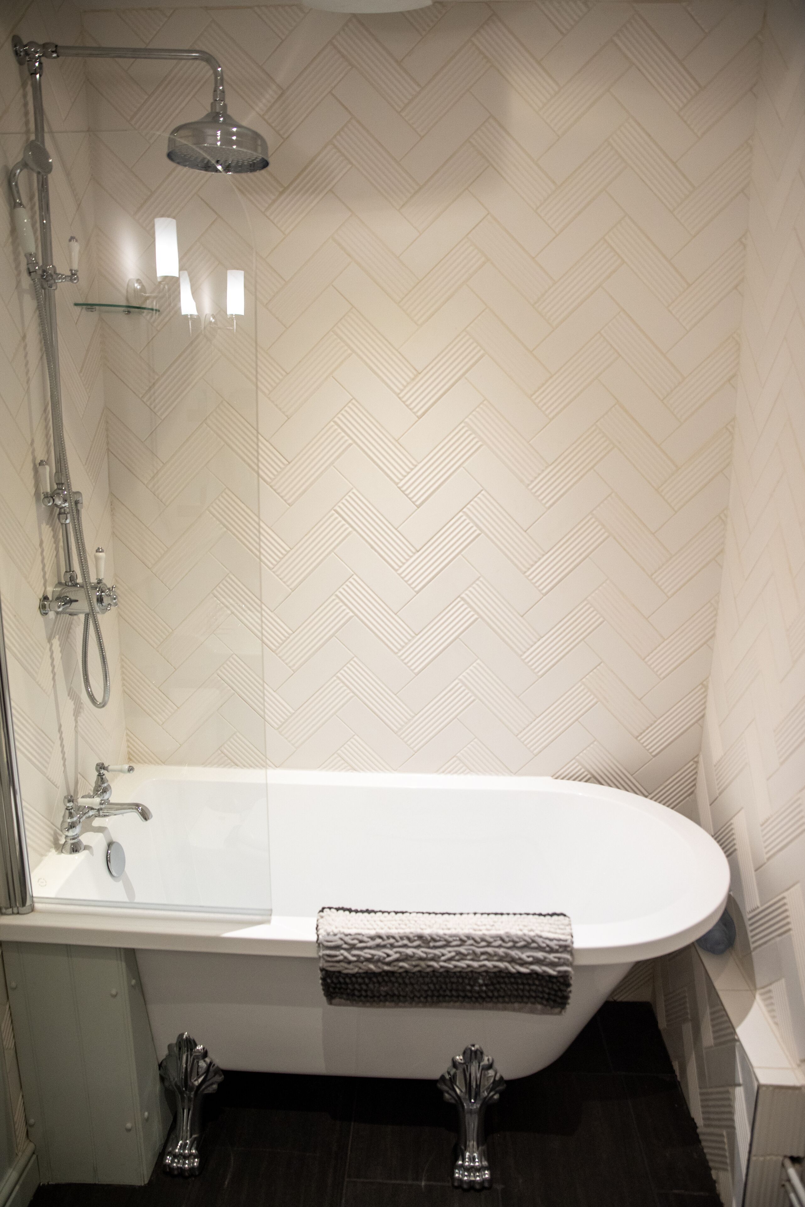 Een badkamer met een vrijstaand bad, een douche met glazen wanden en een wand met een herringbone-patroon.