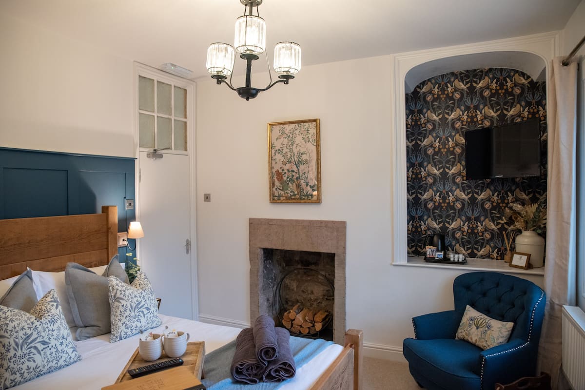 A bedroom with a bed, a blue armchair, a fireplace, and a television mounted on the wall.