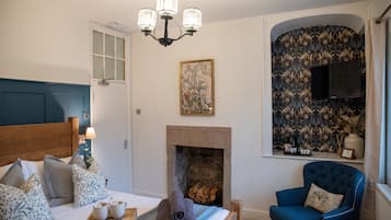 A bedroom with a bed, a blue armchair, a fireplace, and a television mounted on the wall.