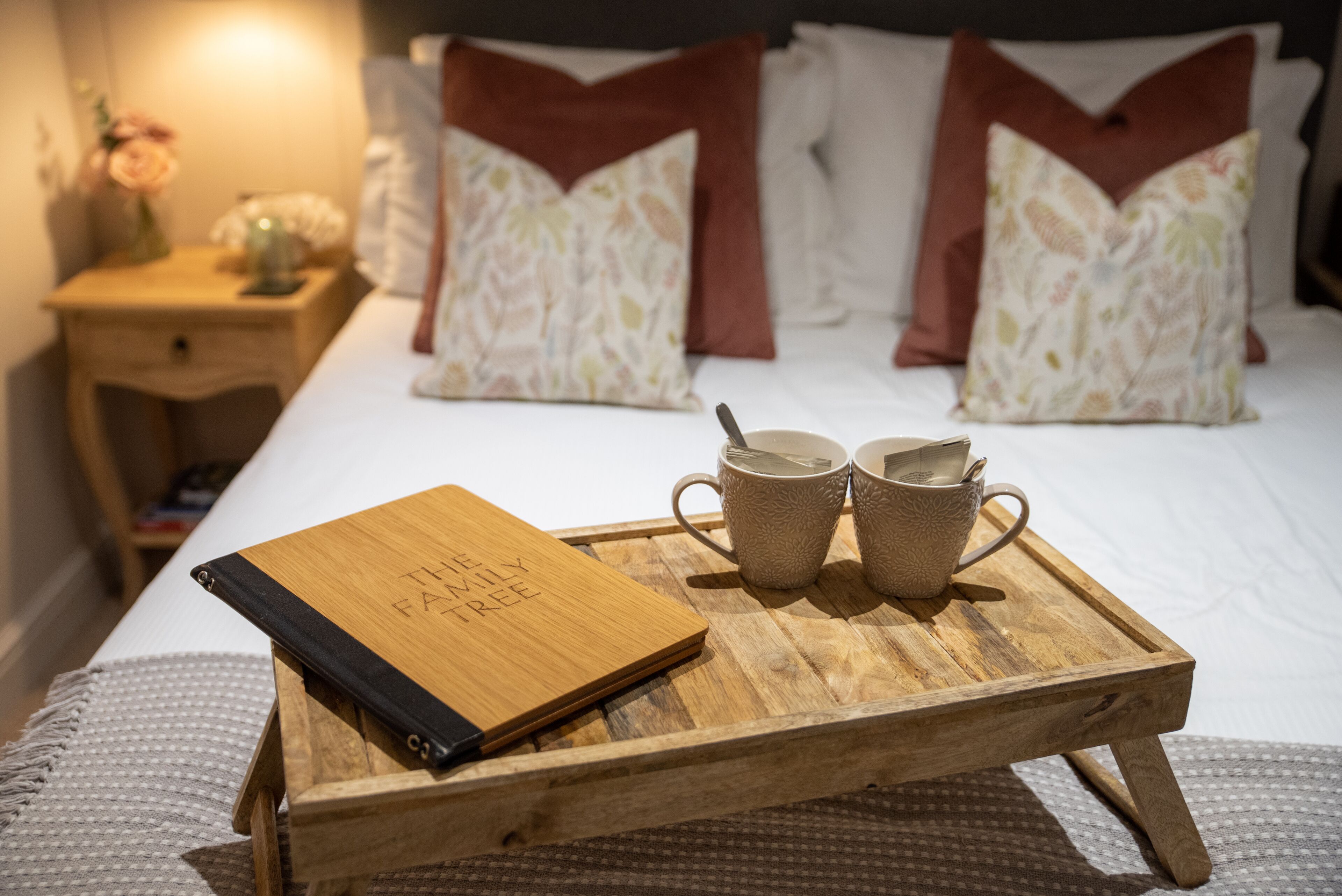 Ein ordentlich bezogenes Bett mit zwei Kissen, ein Nachttisch mit Lampe und ein Tablett mit einem Buch und zwei Tassen.