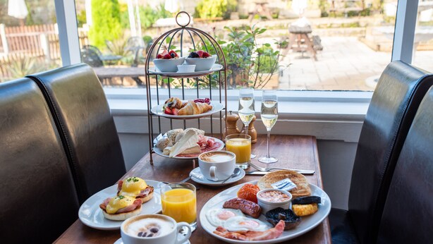 A breakfast table with a variety of dishes, including eggs, toast, and fruit, set in a room with leather chairs and a view of the outdoors. - The Family Tree (Matlock)