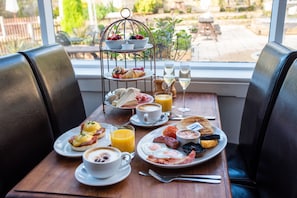 A breakfast table with a variety of dishes, including eggs, toast, and fruit, set in a room with leather chairs and a view of the outdoors. - The Family Tree (Matlock)