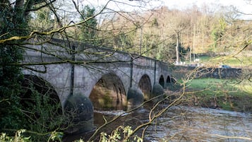 A stone bridge over a river with arches, surrounded by trees and greenery.