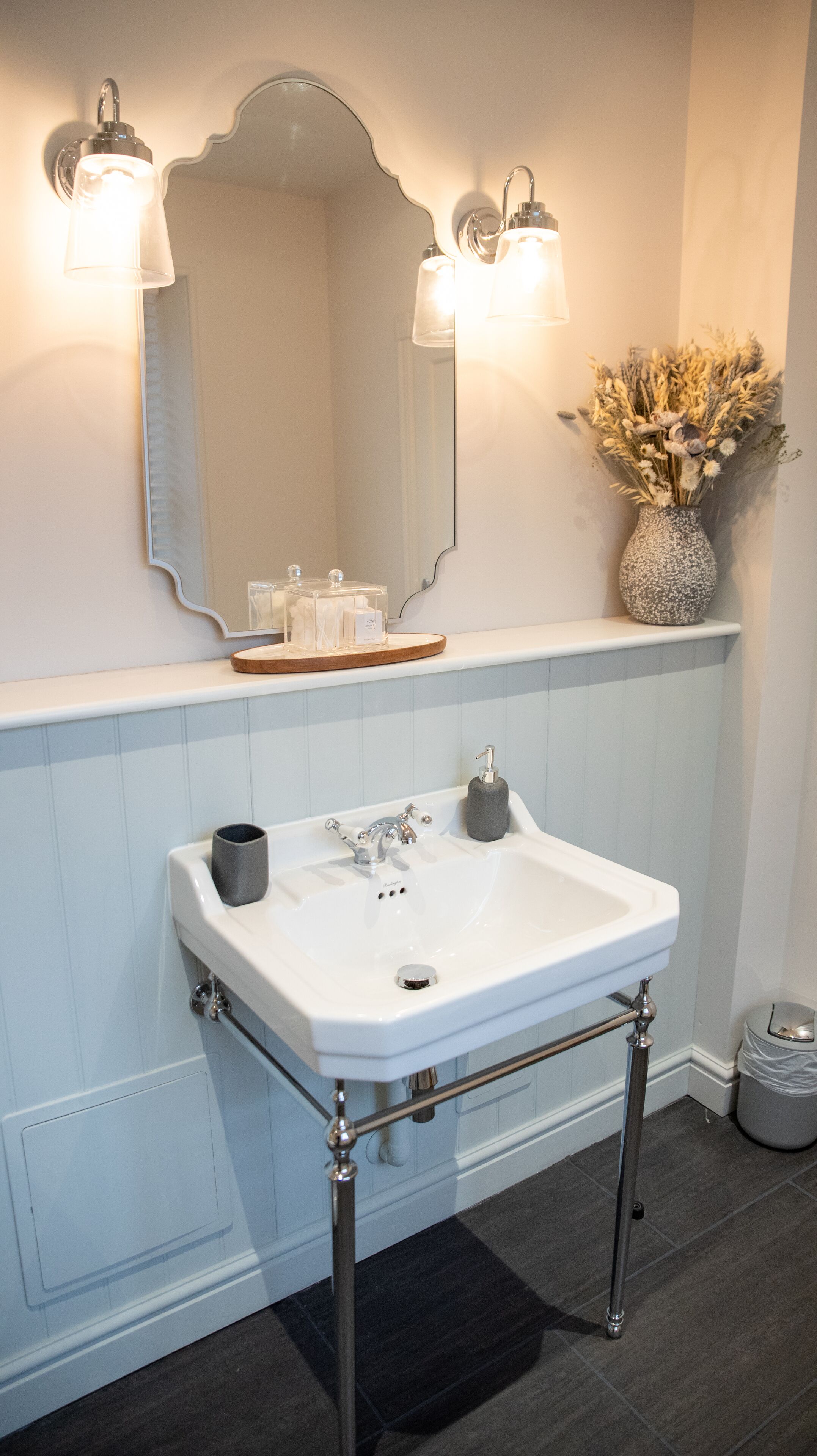 A bathroom with a white sink, chrome fixtures, a mirror, and a vase with dried flowers.