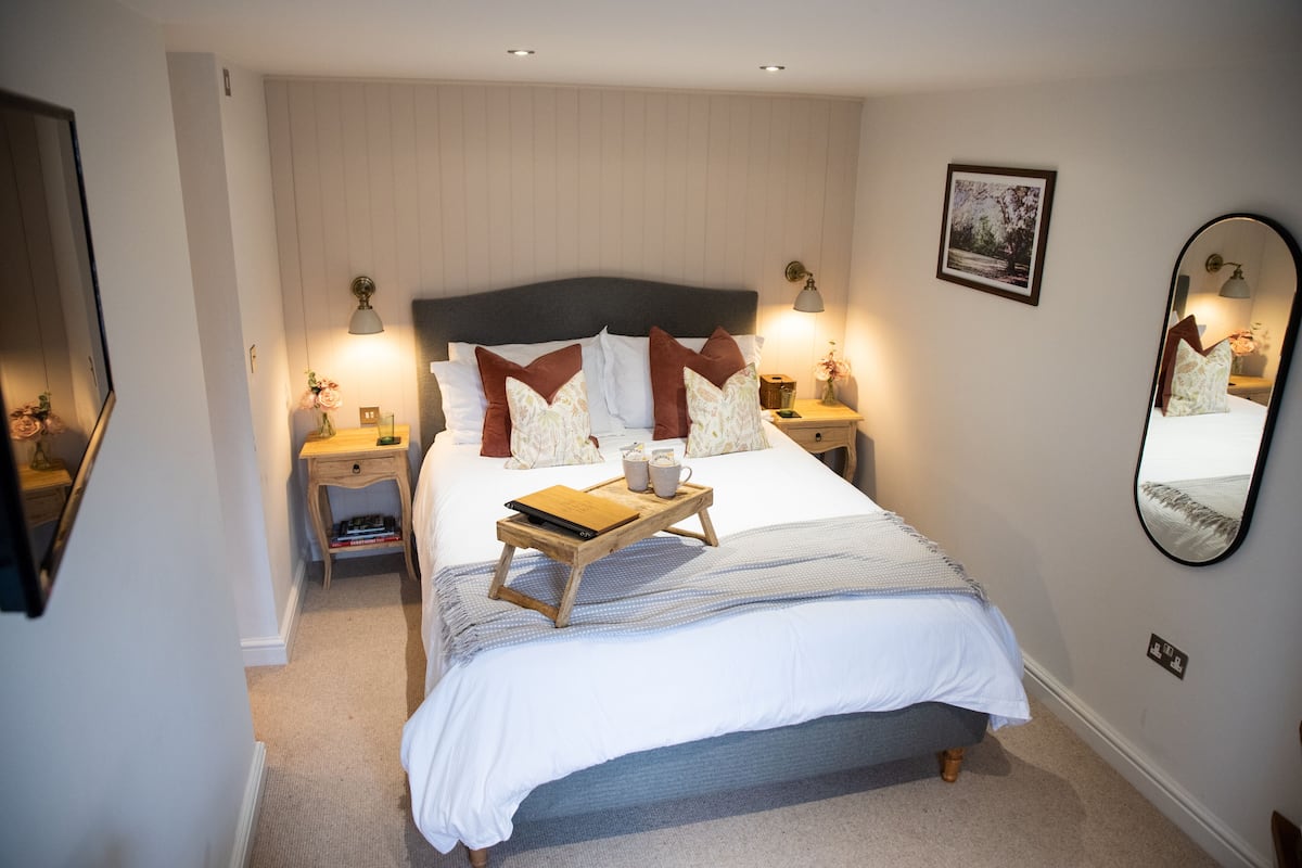 A neatly arranged bedroom with a large bed, bedside tables, a bedside lamp, a mirror, and a framed picture on the wall.
