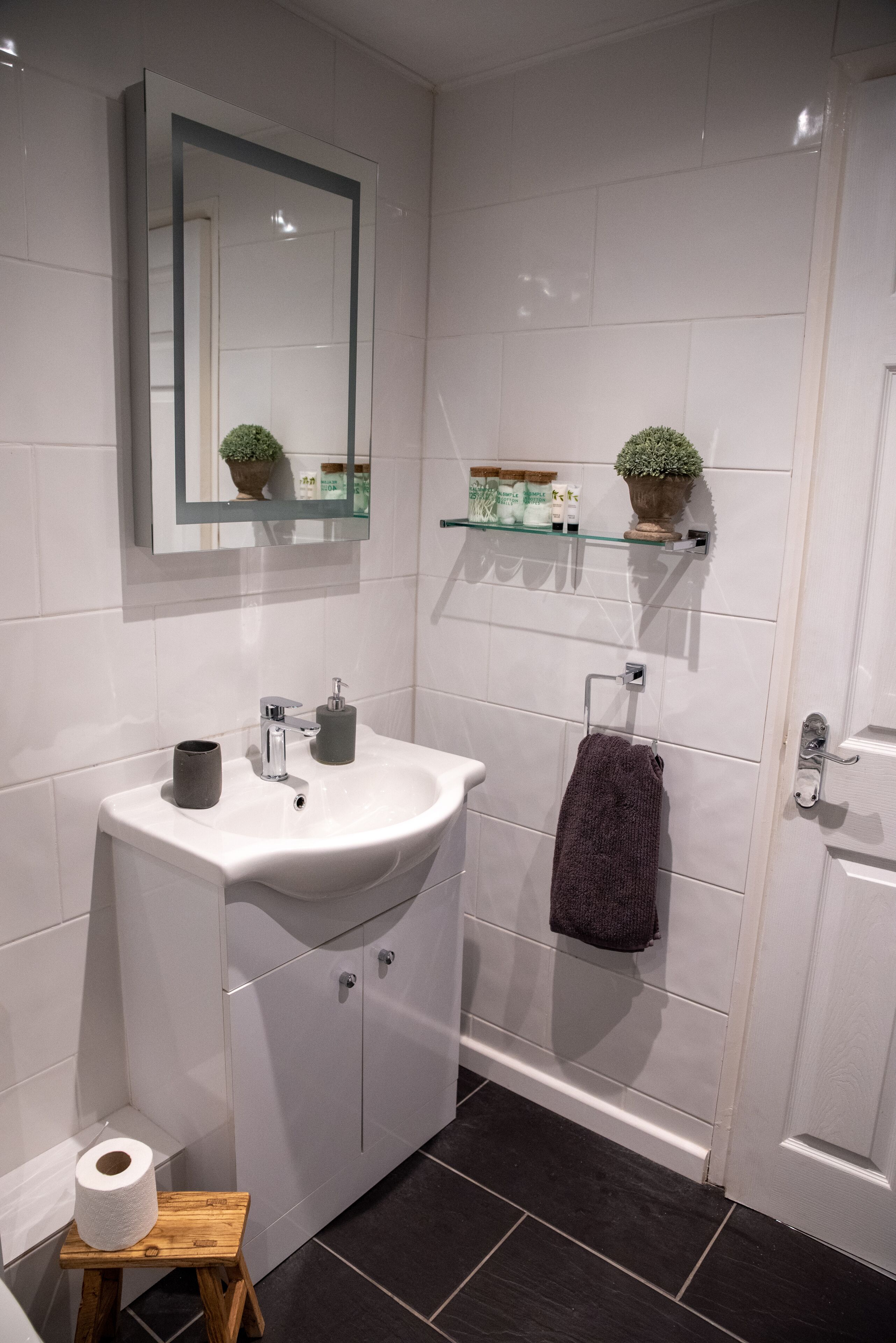 A modern bathroom with a white sink, a mirror, a towel rack, and a small shelf with toiletries.