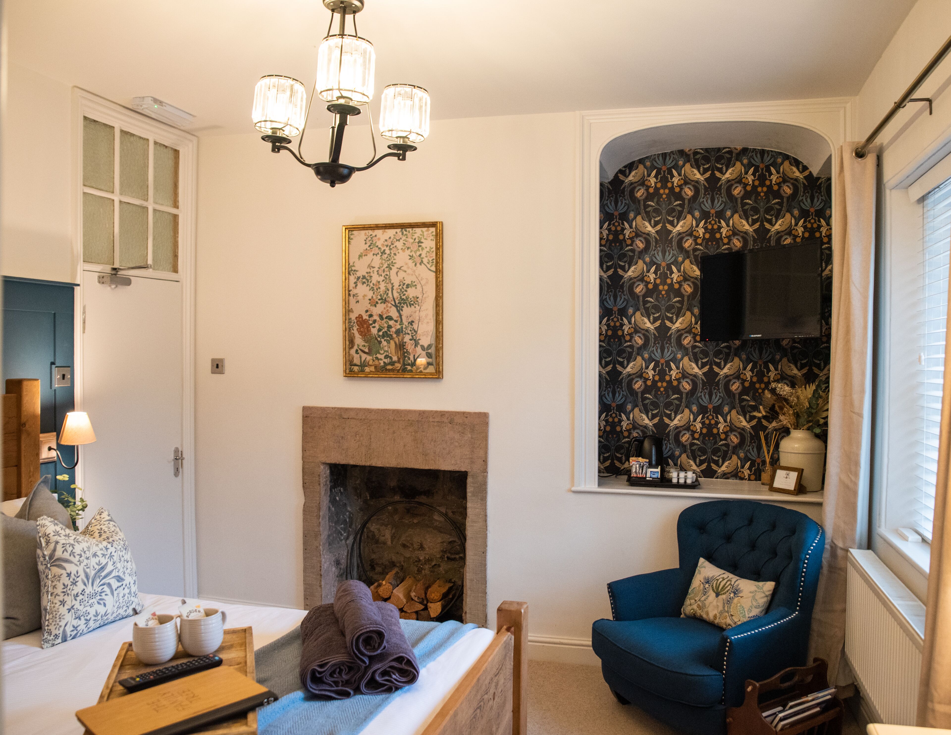 Una habitación con chimenea, un sillón azul, un cuadro y una araña.