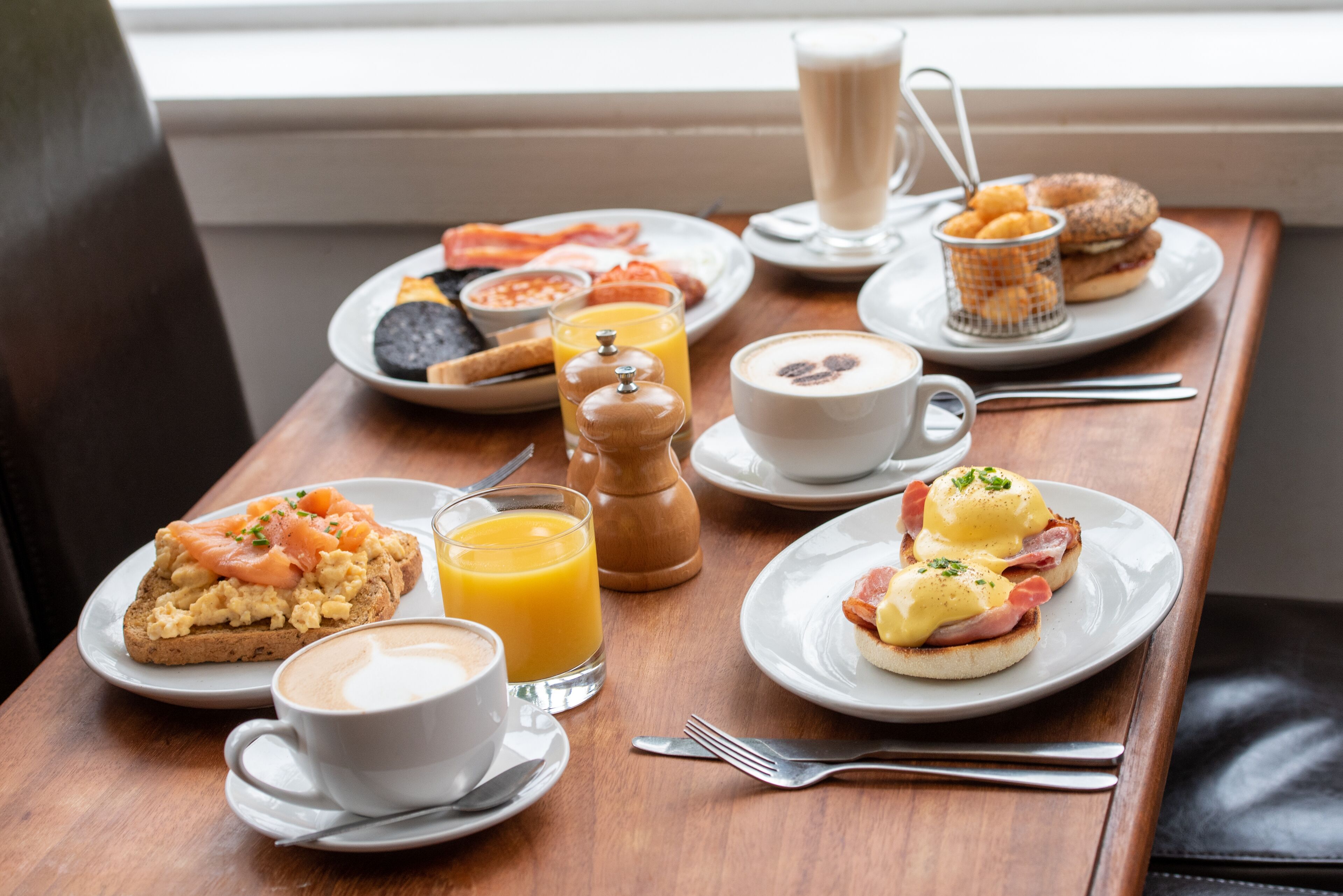 Una mesa de desayuno con diversos platos, incluyendo huevos, tocino y tostadas, junto con tazas de café y jugo de naranja.