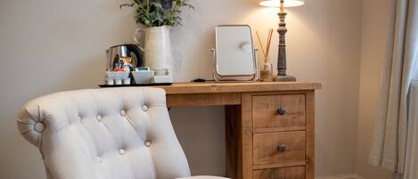 A tufted armchair, a wooden desk with drawers, a lamp, a coffee maker, and a vase with flowers.