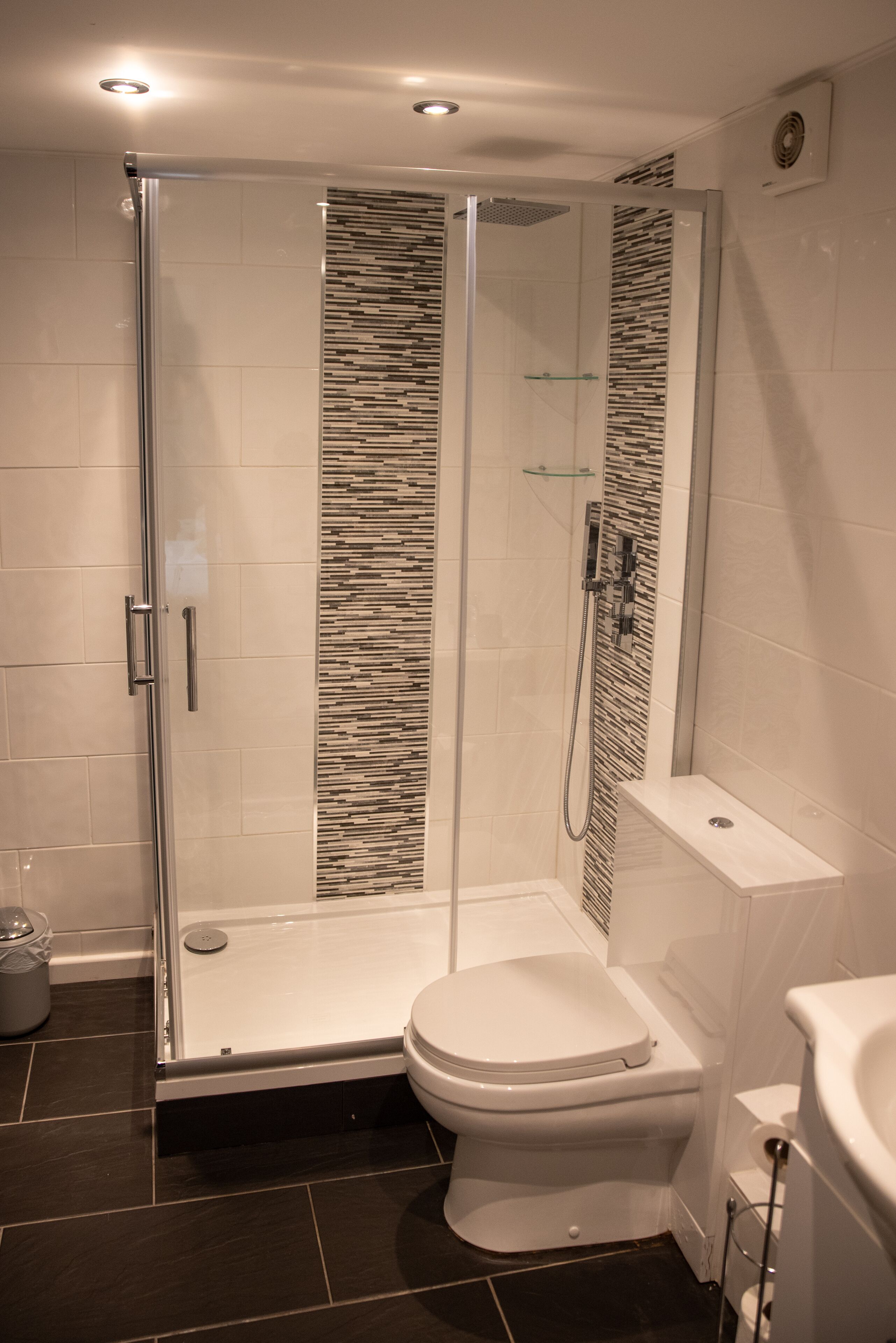 A modern bathroom with a glass-enclosed shower, a white toilet, and a tiled floor.
