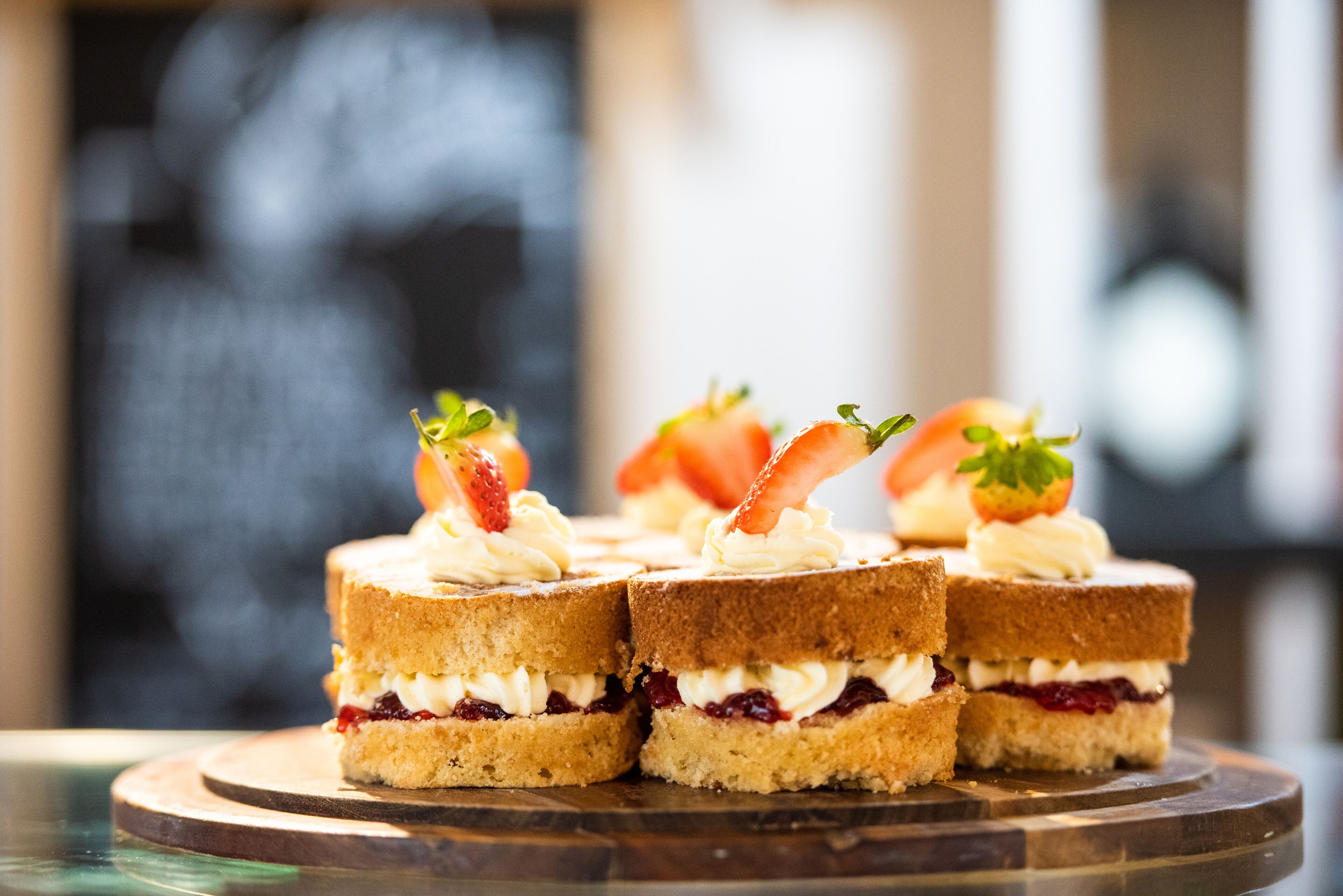 Vier kleine Sandwiches mit Creme und Erdbeeren auf einem Holzboden.