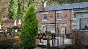 A stone building with a brick facade, a wooden deck, and outdoor seating. - The Family Tree (Matlock)