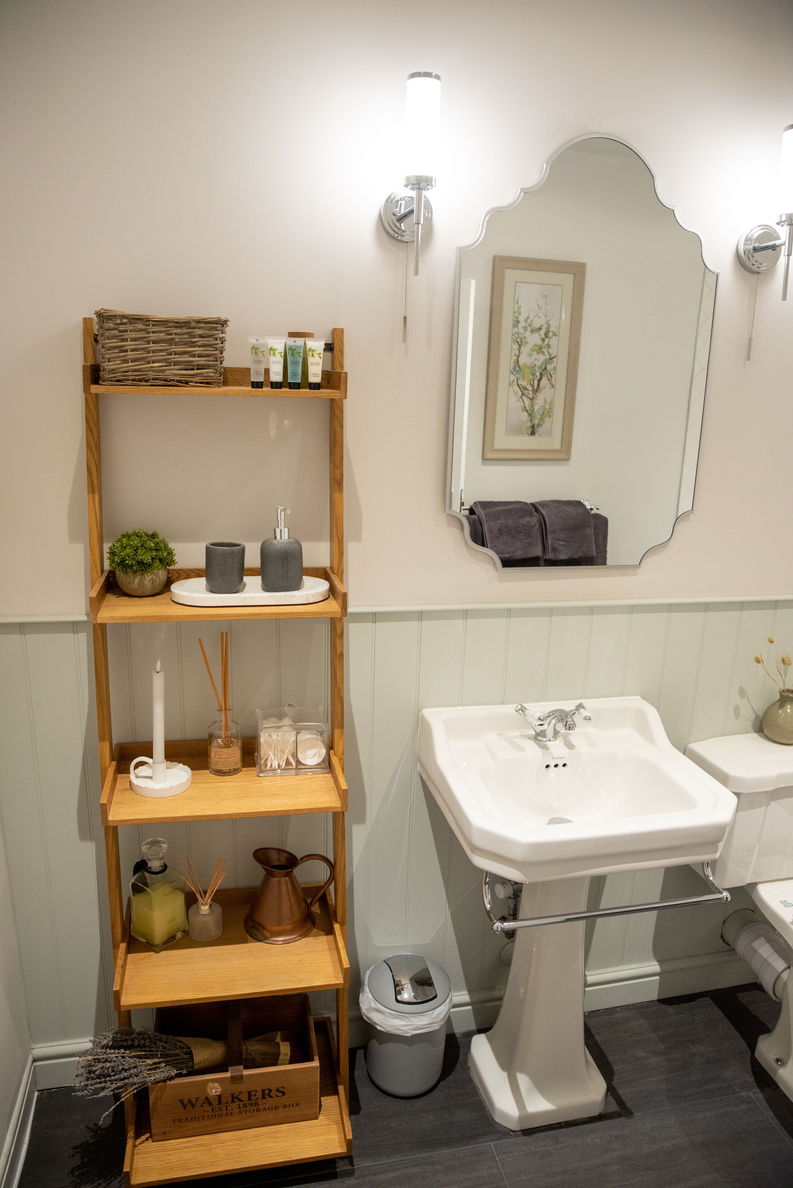 A bathroom with a white sink, a mirror, and shelves with toiletries.