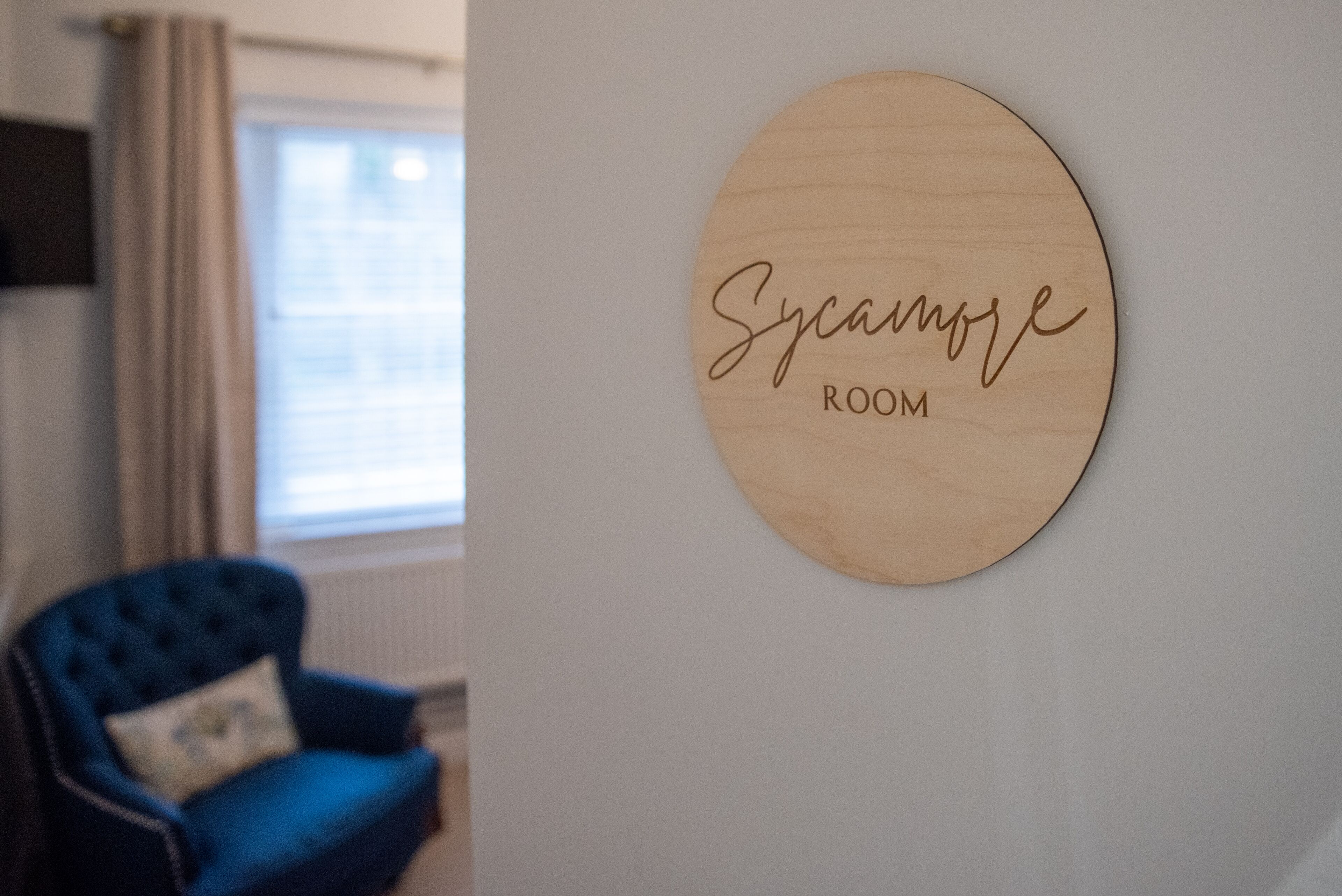A room with a blue armchair and a wooden sign that reads "Sycamore Room."
