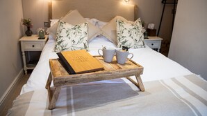 A neatly made bed with a wooden tray holding a book and two mugs, flanked by matching pillows and bedside tables with lamps. - The Family Tree (Matlock)