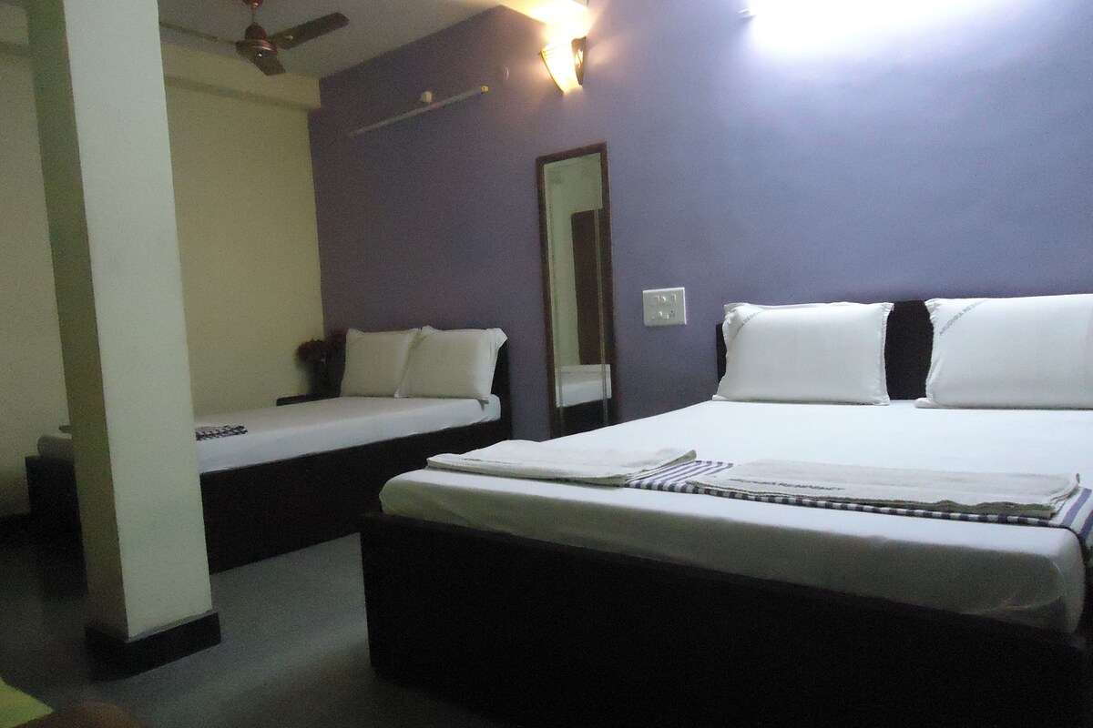 A hotel room with two single beds, a large bed, a mirror, and a ceiling fan.