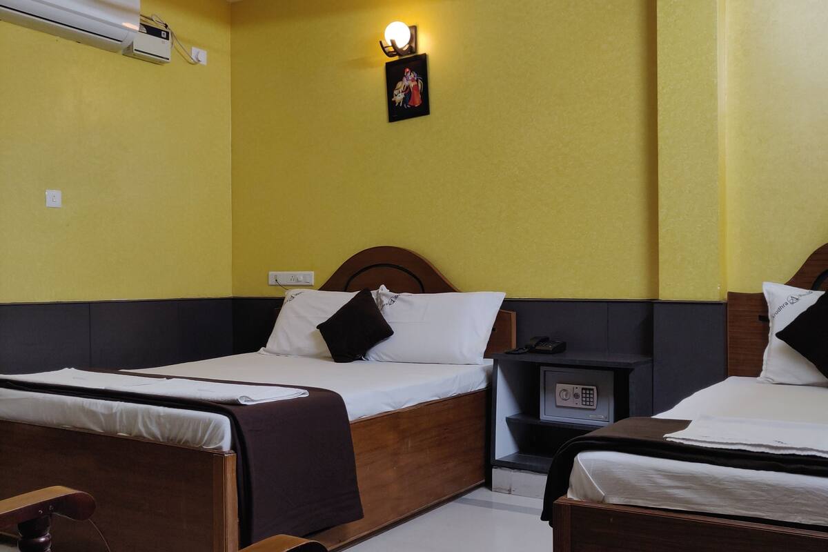 A hotel room with two single beds, a bedside table with a phone, a wall-mounted heater, and a ceiling fan.