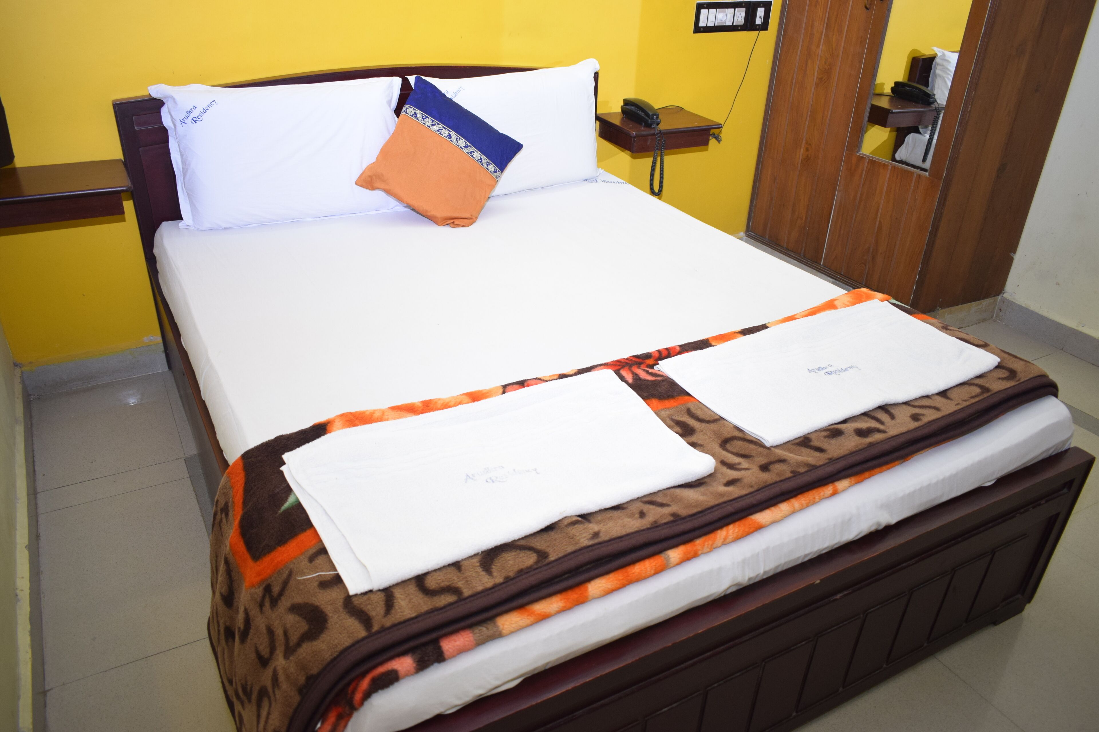 Een opgemaakt bed met een beddengoed met patroon, een wit kussen en een oranje kussen.