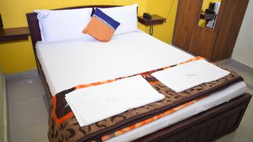 Een opgemaakt bed met een beddengoed met patroon, een wit kussen en een oranje kussen.