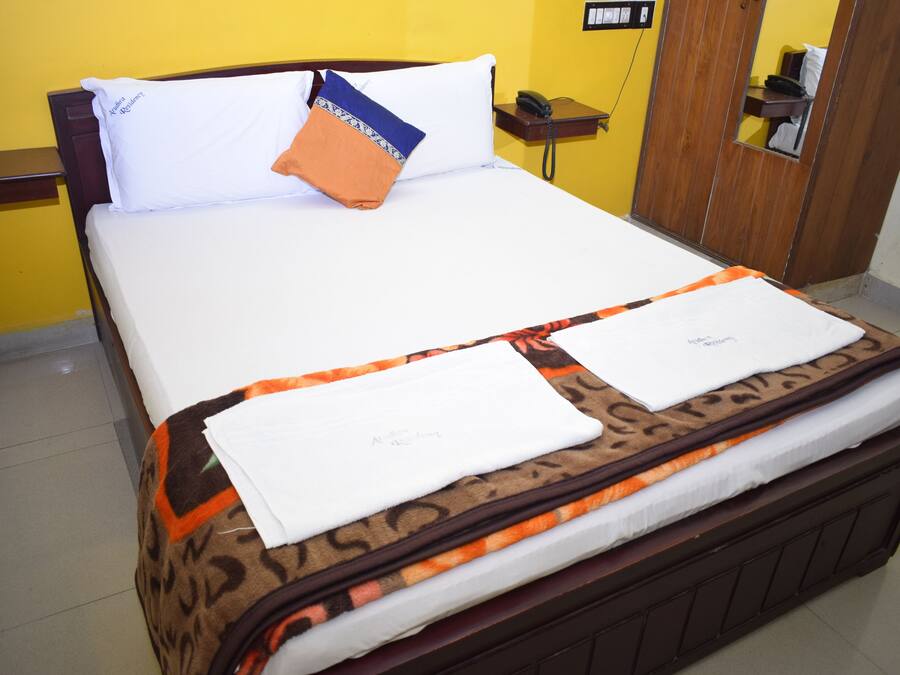 Een opgemaakt bed met een beddengoed met patroon, een wit kussen en een oranje kussen.
