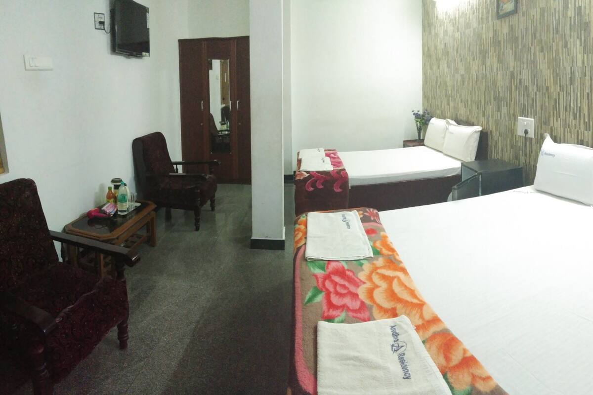 A hotel room with a large bed, two smaller beds, a desk, a chair, a mirror, and a wooden wall panel.