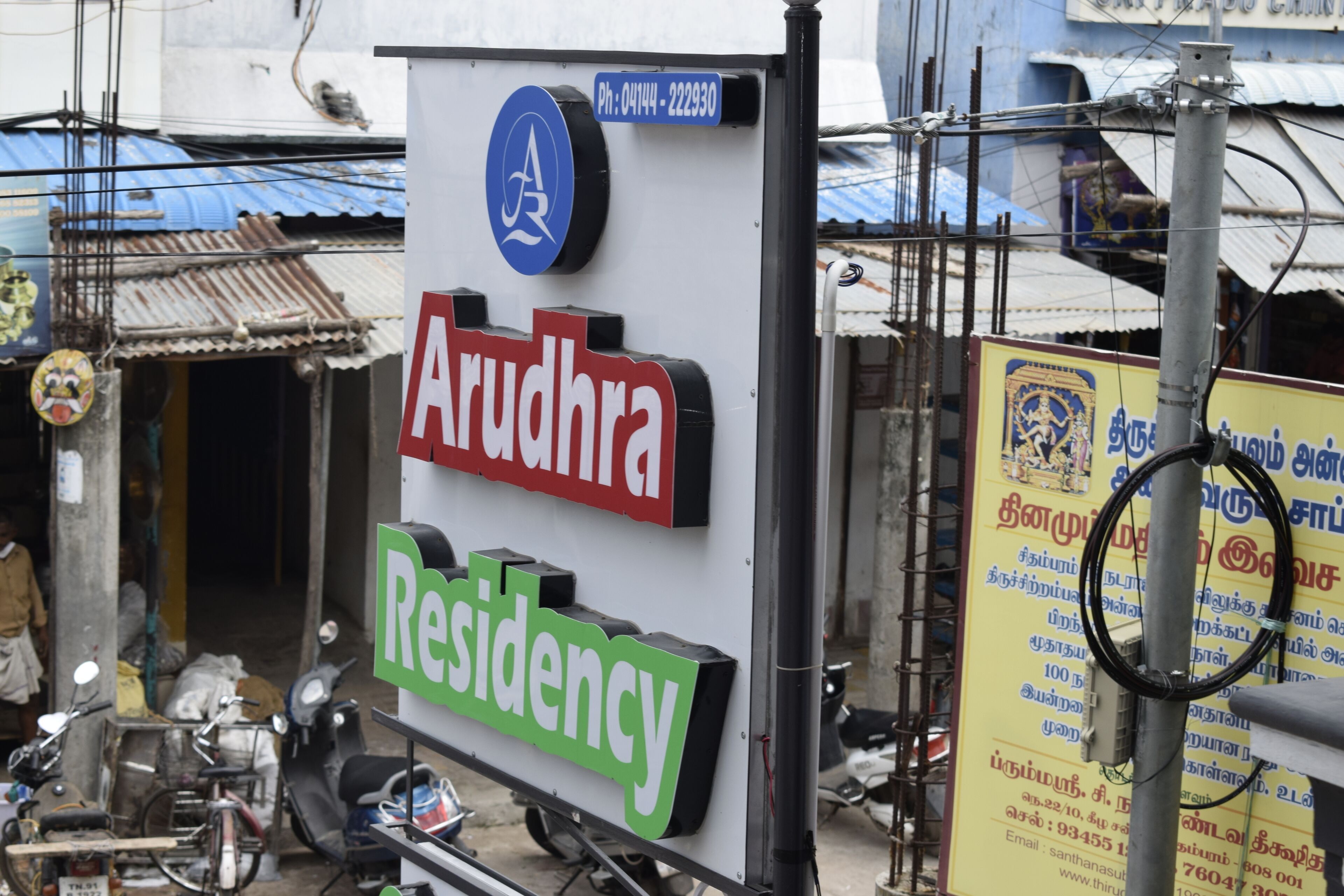 A sign for 'Arudhra Residency' with a contact number and a logo.