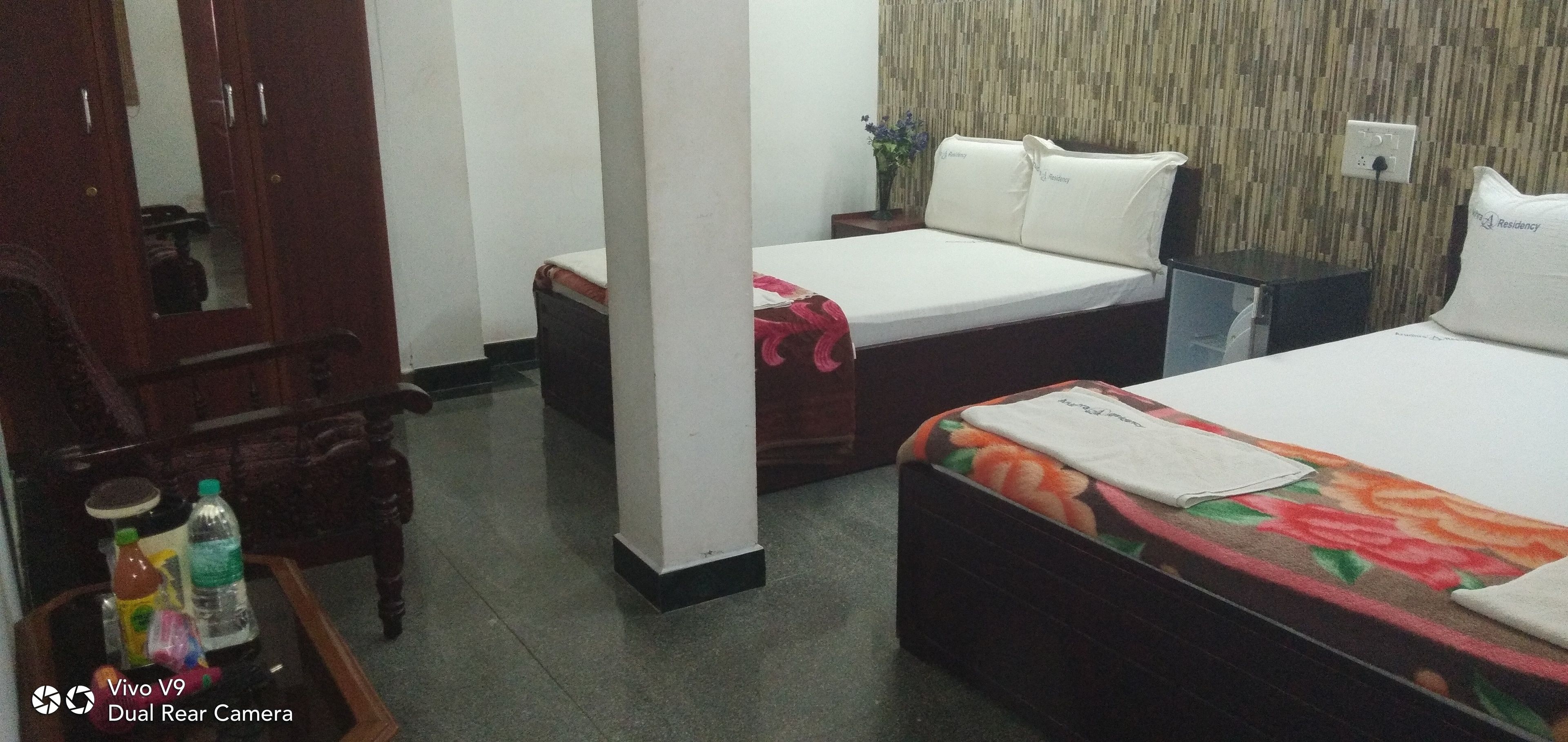 A hotel room with two single beds, a wooden wardrobe, a small table with a bottle and a water bottle, and a mirror on the wardrobe door.