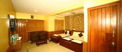 A hotel room with a large bed, a desk with a chair, a small sofa, and a wooden wardrobe.