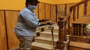 Una persona usando un dispensador de gel hidroalcohólico en una escalera de madera con barandales decorativos.