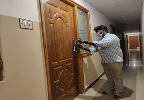 A person in a checkered shirt and khaki pants opening a wooden door with intricate designs. - Arudhra Residency (Chidambaram)