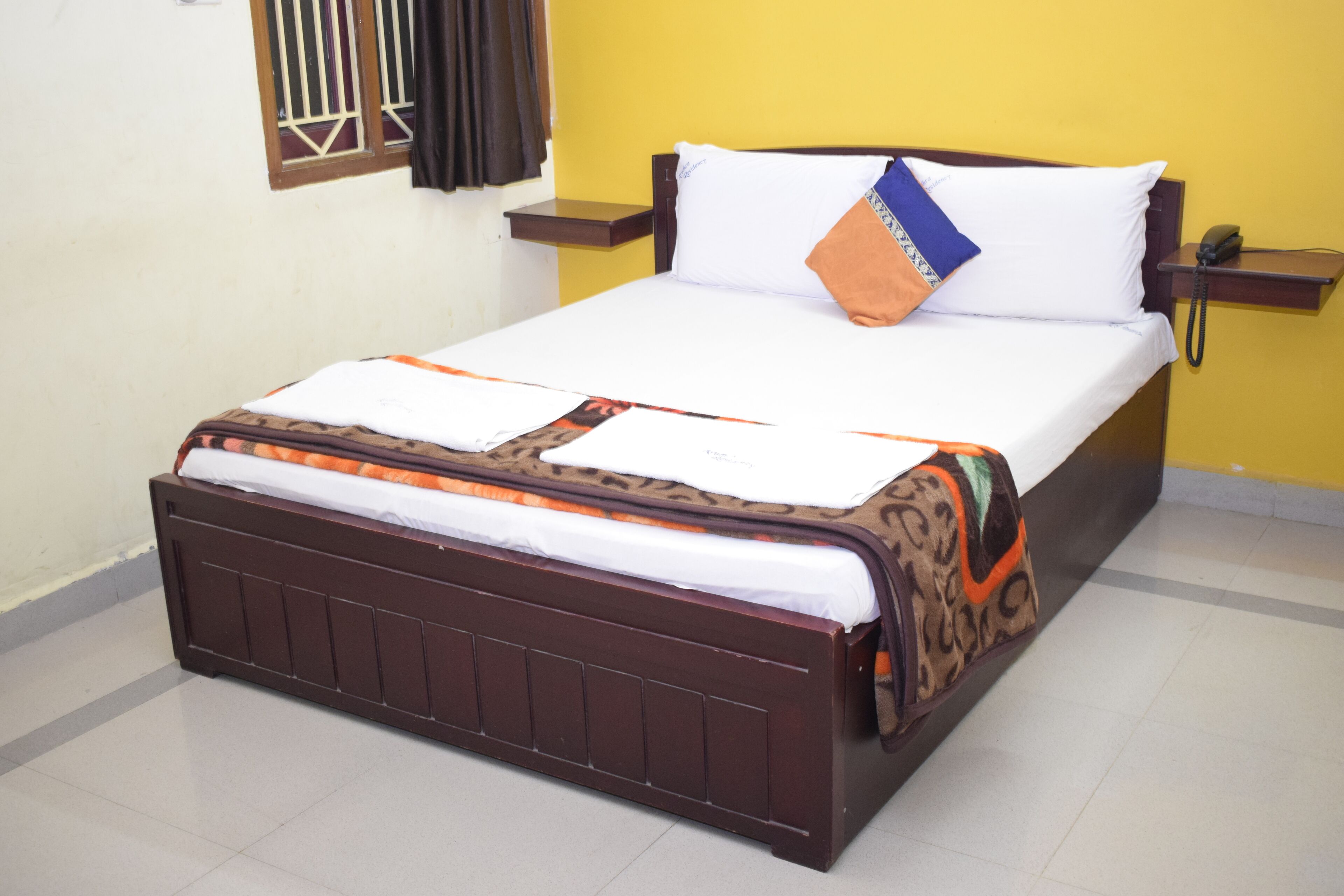 Una cama con una colcha estampada, una almohada con diseño azul y naranja, y un teléfono en la mesita de noche.