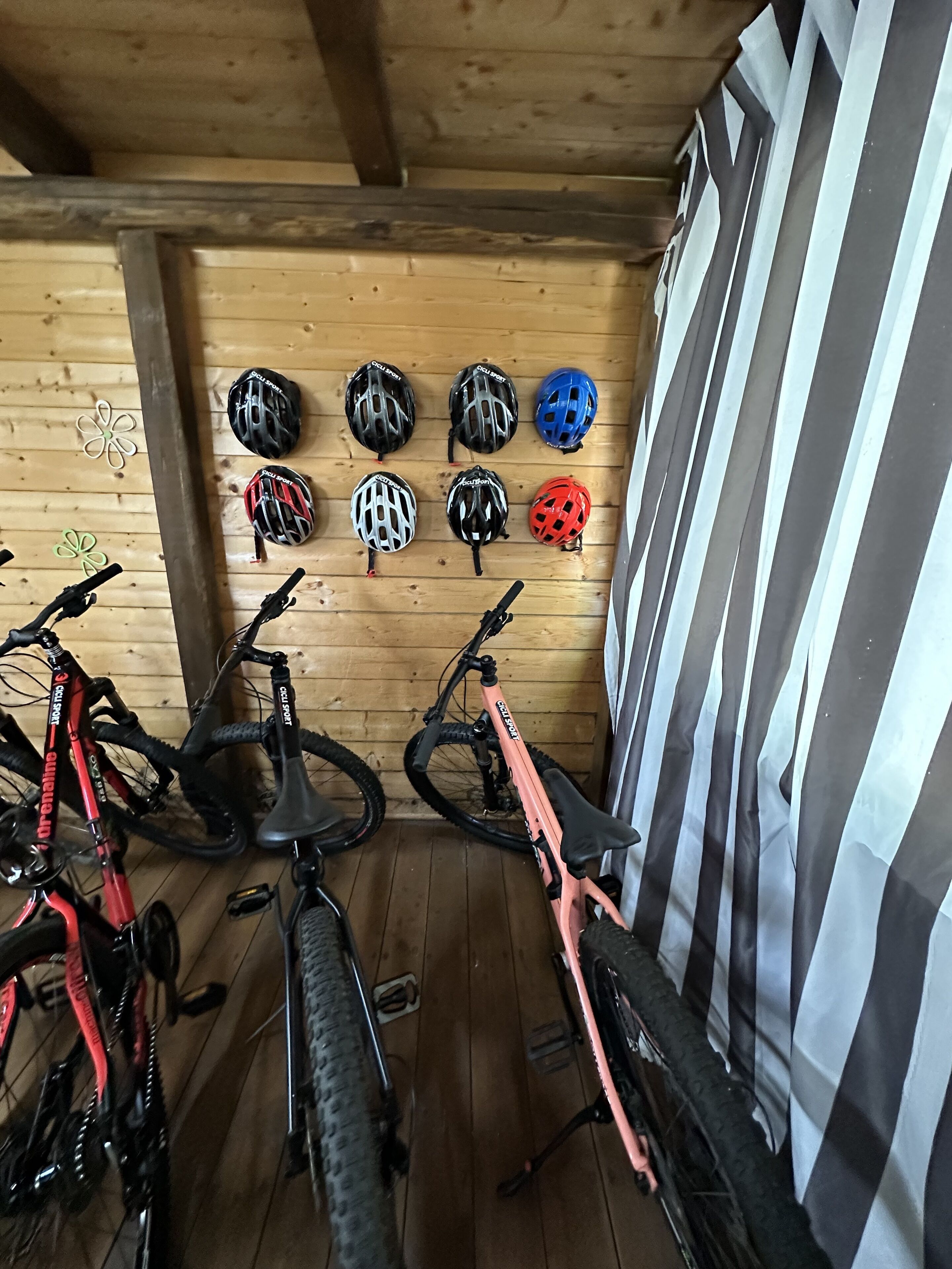 Una habitación con paredes de madera y techo inclinado. Se ven bicicletas y cascos en la pared.