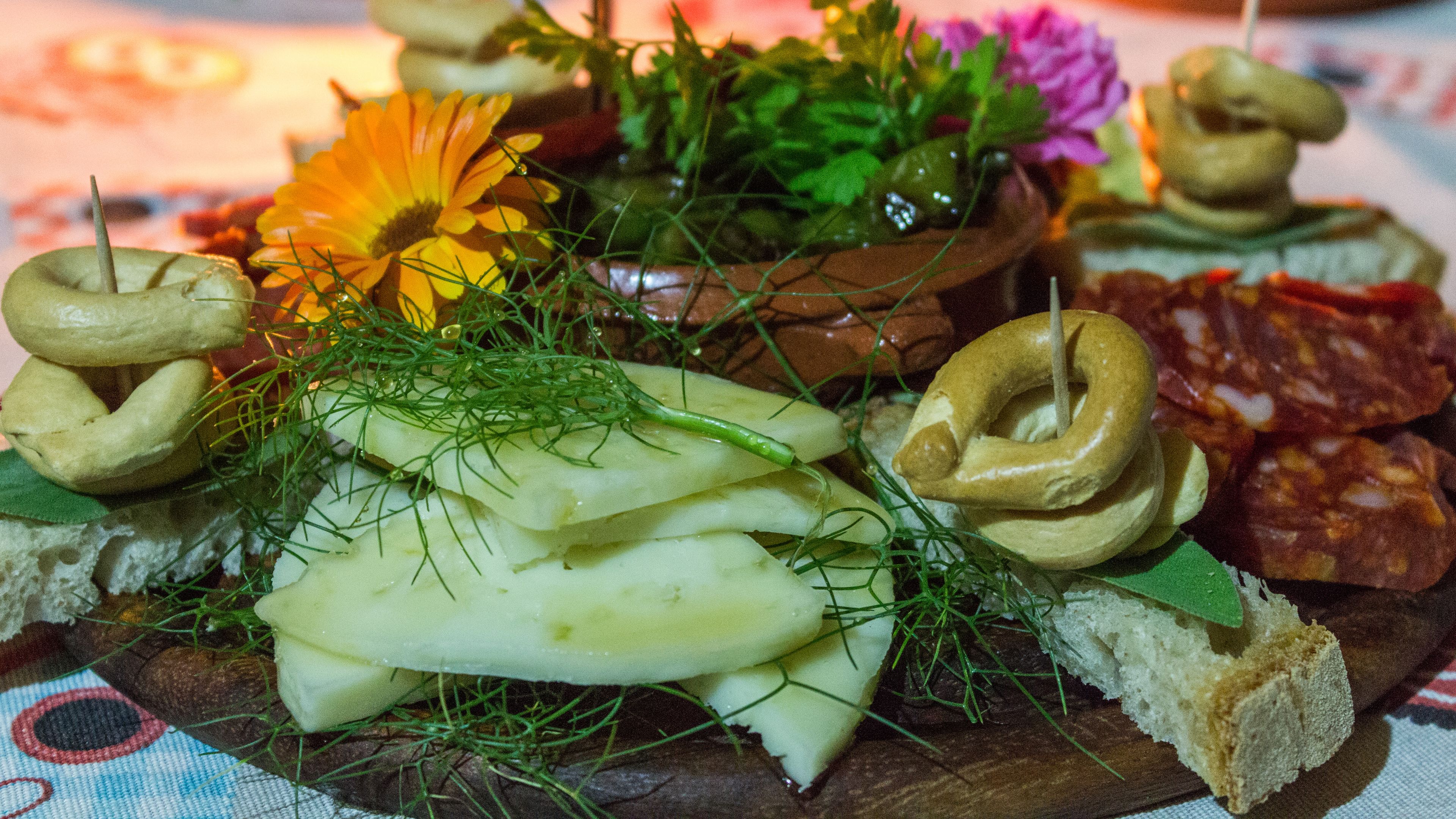 Une planche en bois sur laquelle sont disposés divers aliments, notamment du pain, du fromage et une fleur.