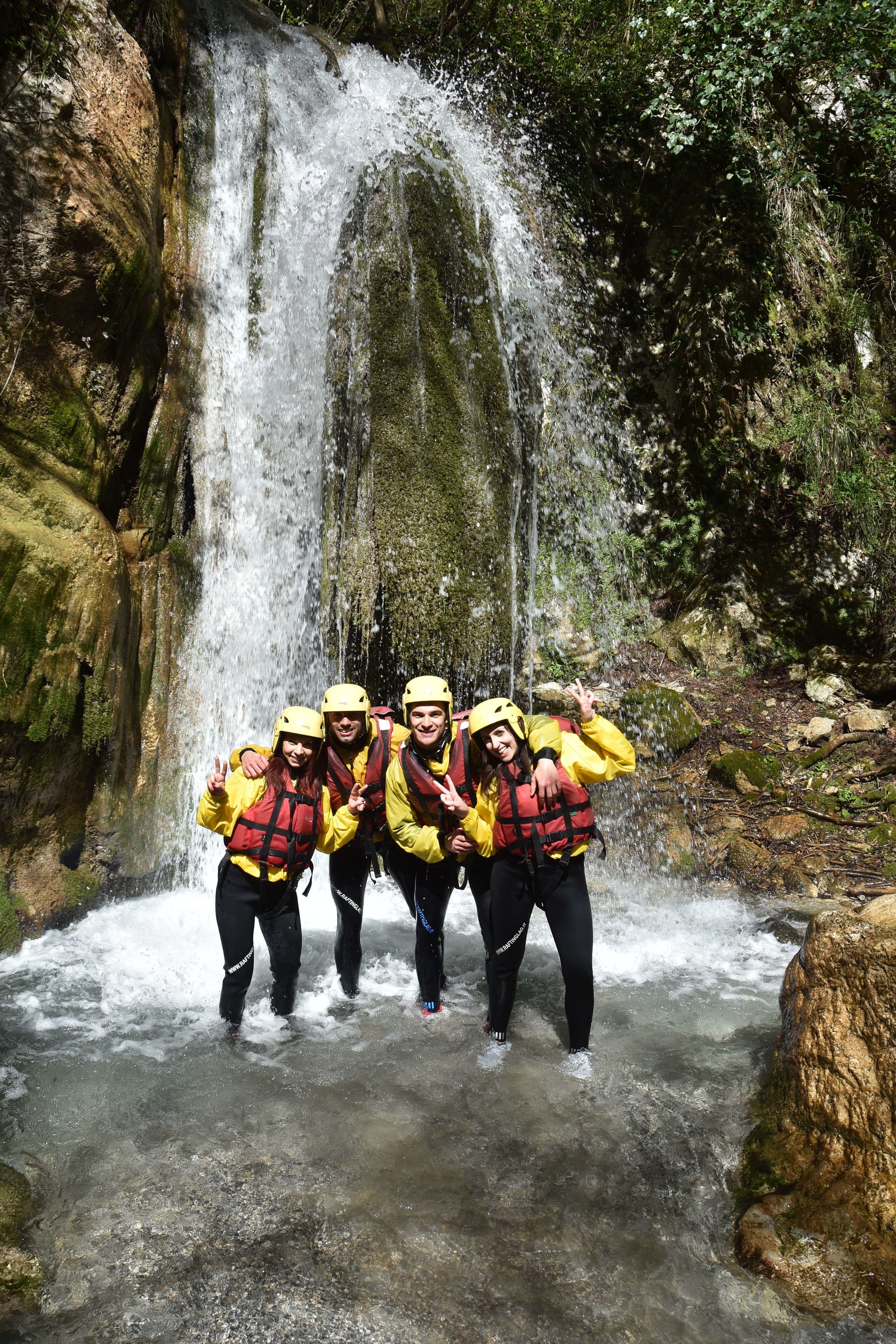 A group of people in yellow jackets and helmets standing in a stream with a waterfall in the background.