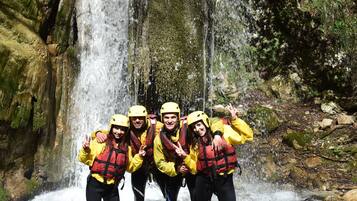 A group of people in yellow jackets and helmets standing in a stream with a waterfall in the background.