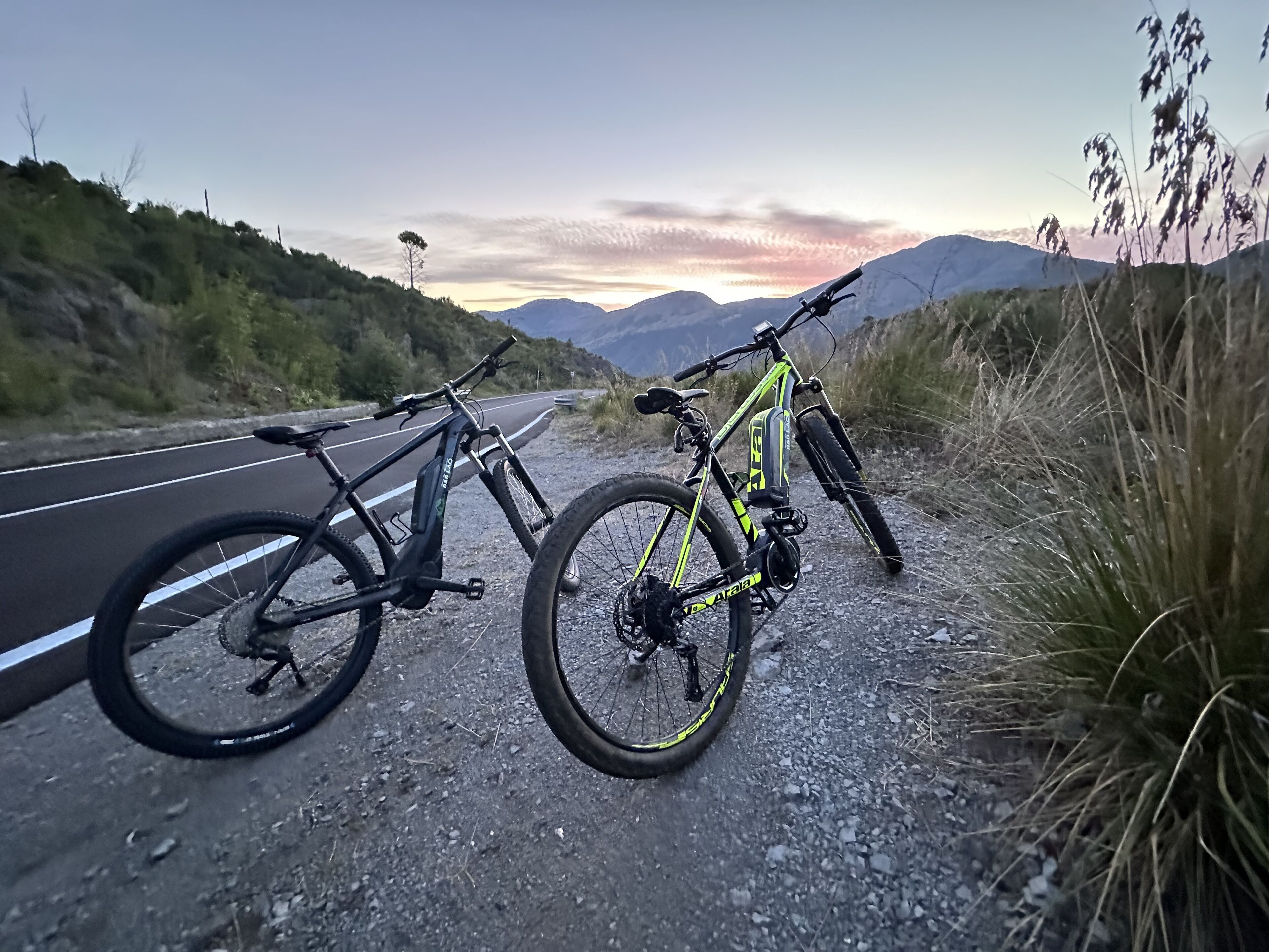 Two bicycles parked on a road with a mountainous backdrop.
