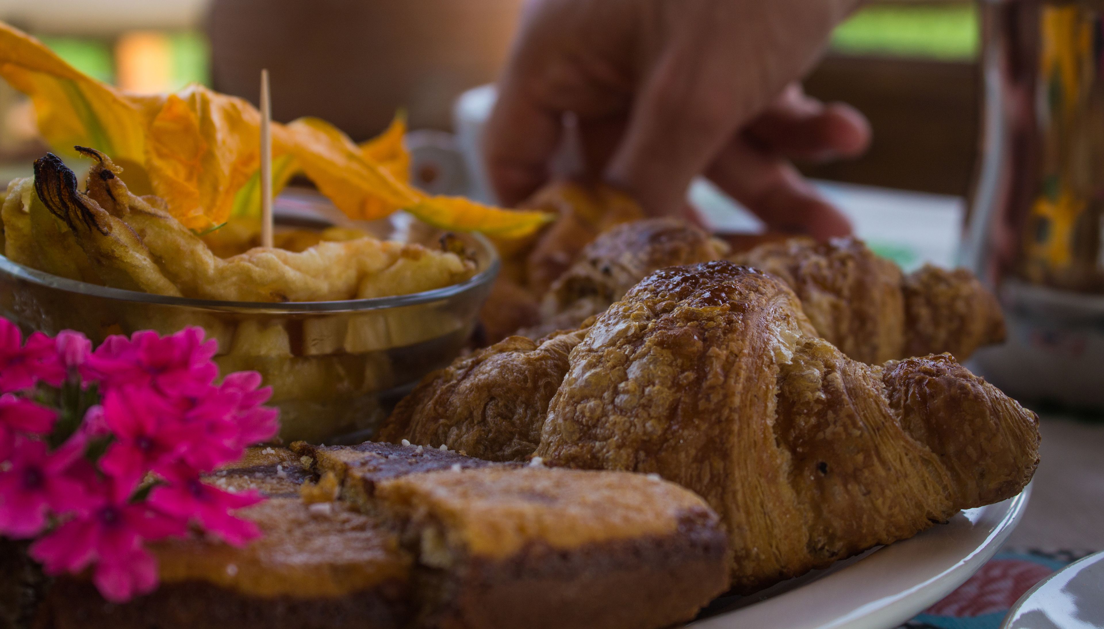 Un plato de comida que incluye croissants y un bol de alimentos fritos, con una flor rosa en primer plano.