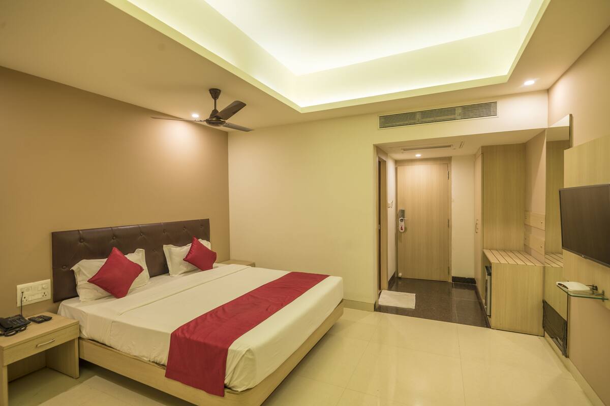 A hotel room with a bed, a nightstand, a ceiling fan, a TV, and a bathroom door.