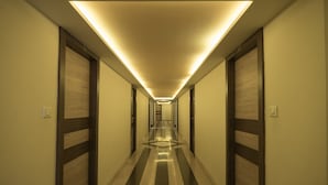 A long, narrow hotel corridor with a striped floor, wooden doors, and a ceiling light fixture. - Hotel Nisarga (Bhopal)