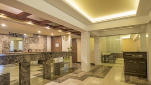 A hotel lobby with a reception desk, a clock, and a check-in/out sign. - Hotel Nisarga (Bhopal)