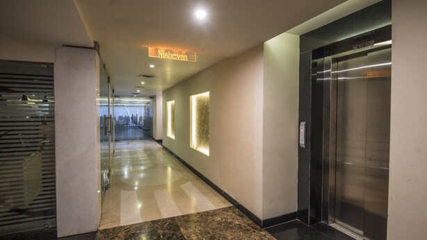 A modern hallway with a glass door, a sign reading "Nishevan", and an elevator. - Hotel Nisarga (Bhopal)