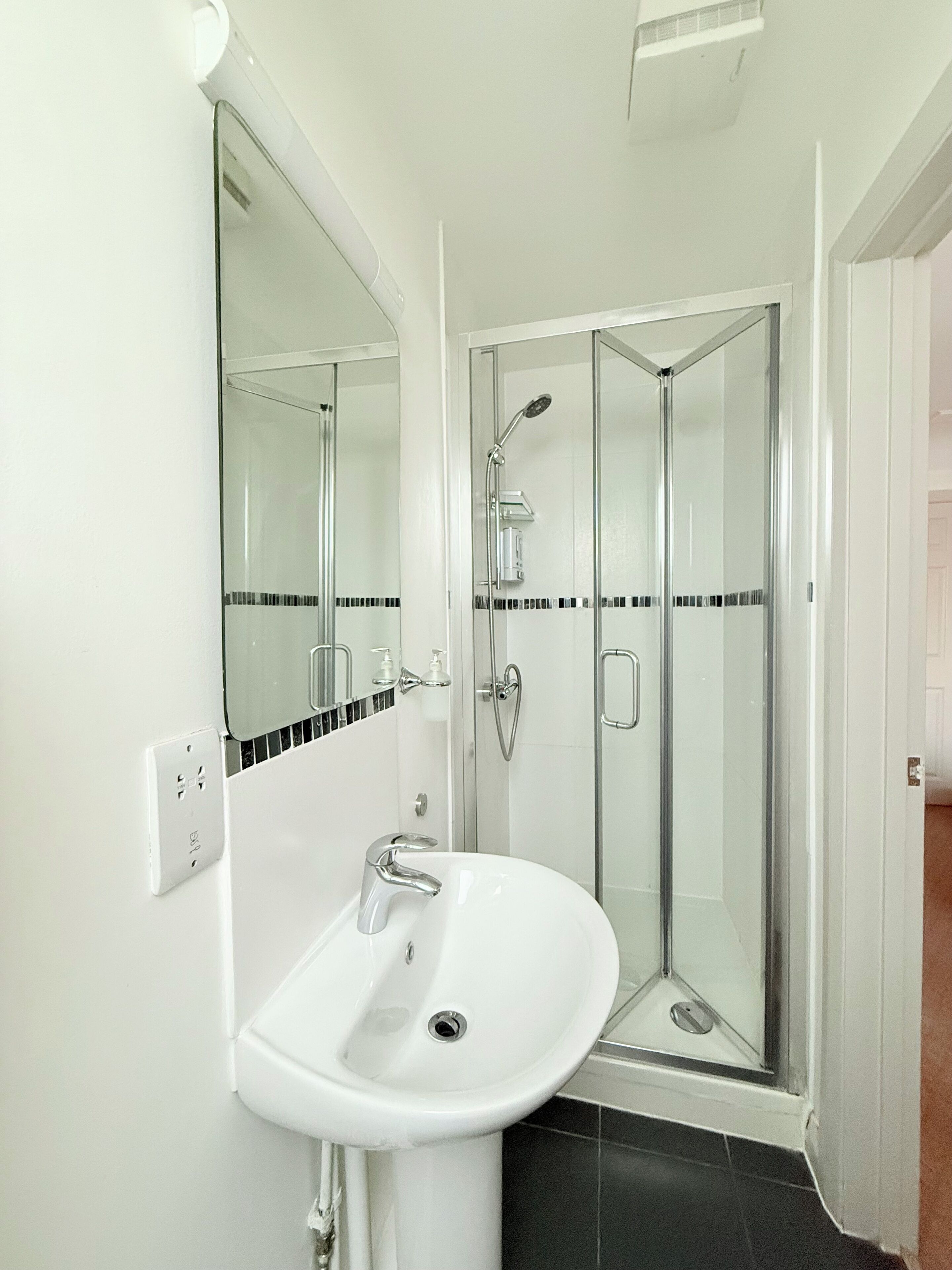 A bathroom with a white sink, a glass shower enclosure, and a mirror above the sink.