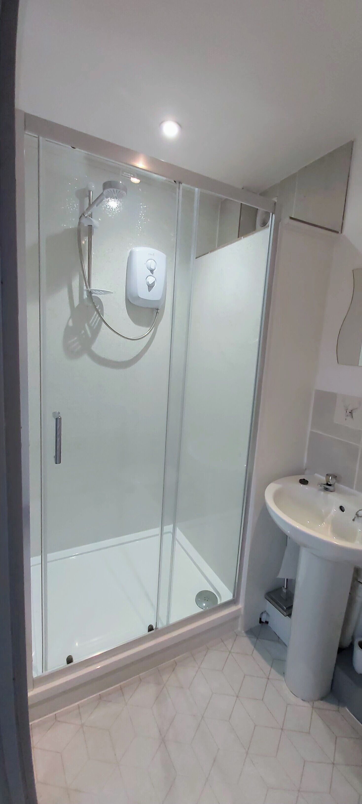 A modern bathroom with a glass-enclosed shower, a white sink, and a tiled floor.