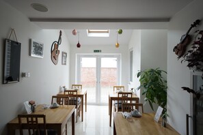 A dining area with wooden tables and chairs, a piano, and a violin on the wall.