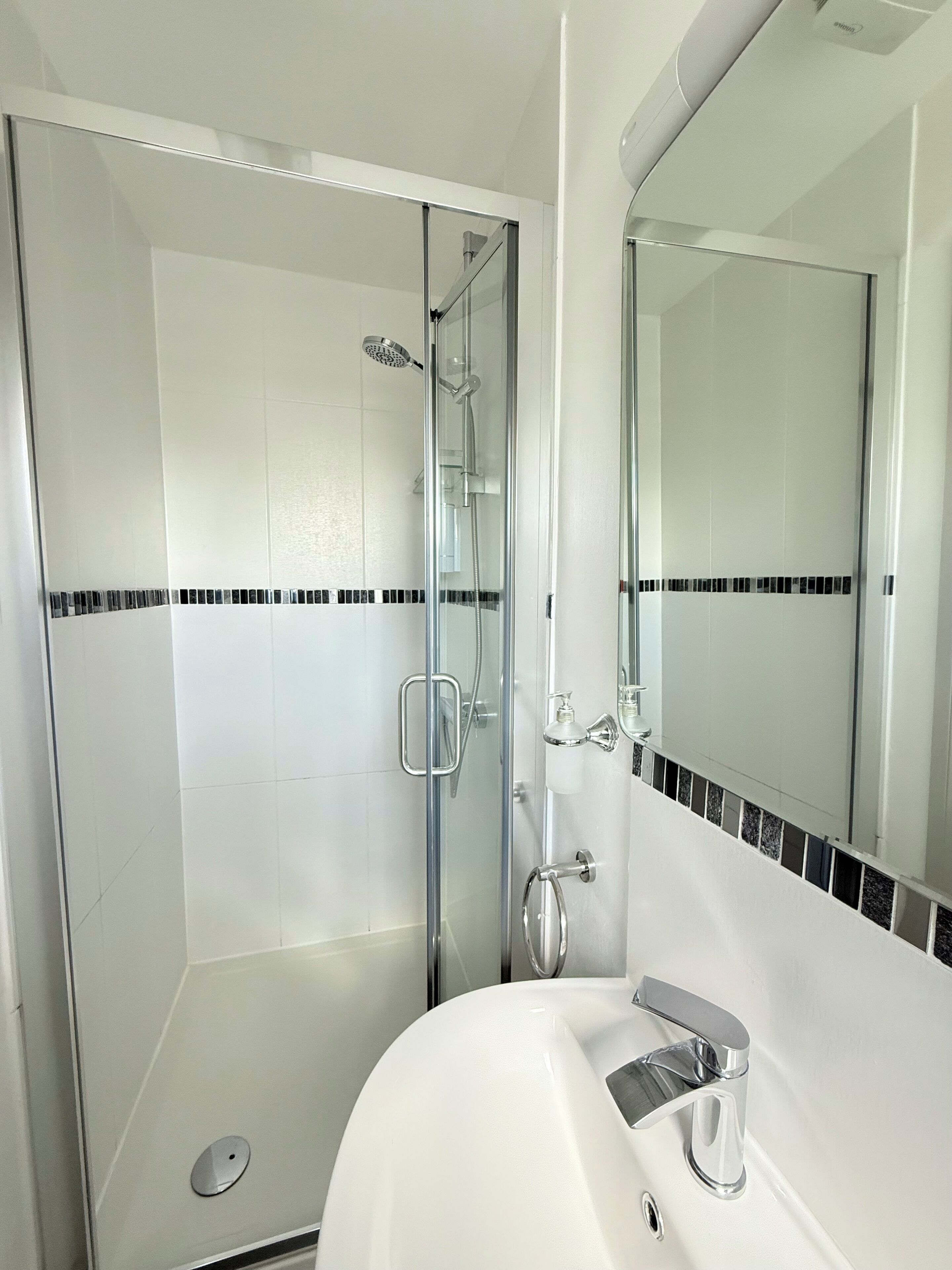 A modern bathroom with a glass-enclosed shower, a white sink, and a mirror above it.