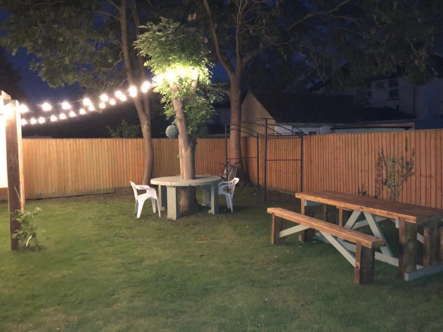Un jardin avec une clôture en bois, une table ronde entourée de chaises et une table de pique-nique.